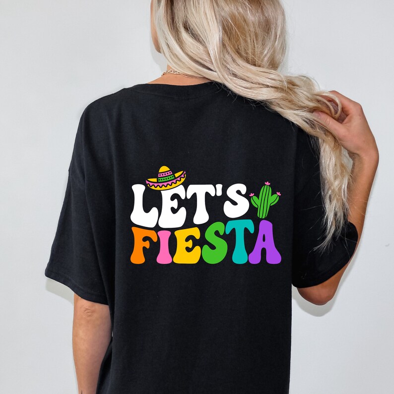 May include: Black t-shirt with a white graphic that says "Let's Fiesta" in rainbow colors. The graphic also includes a cartoon sombrero and cactus.