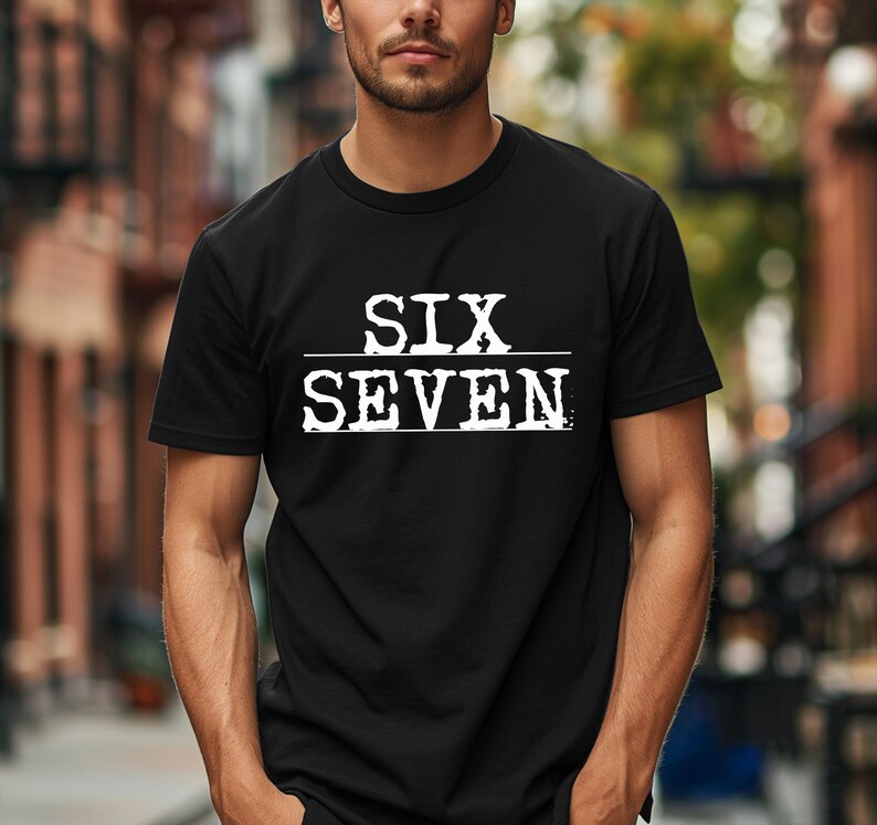May include: Black crew neck t-shirt with the white text "SIX SEVEN" printed across the chest. The text is separated by a horizontal line. The shirt is made of a soft material.