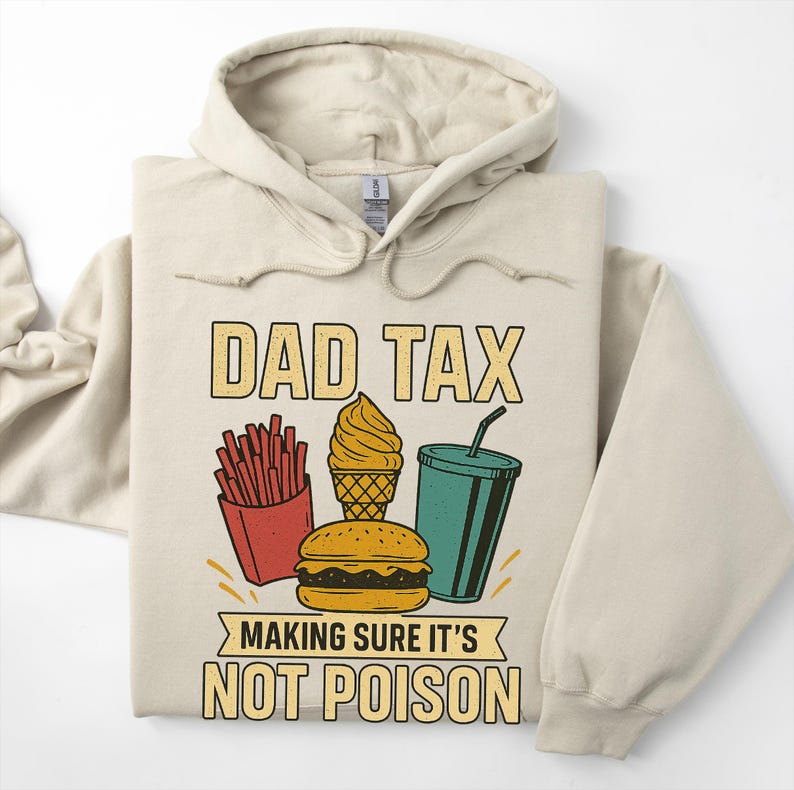 May include: Beige hoodie featuring the text "DAD TAX" and a graphic of fast food items: fries, ice cream, a burger, and a drink. The text "MAKING SURE IT'S NOT POISON" is below the graphic. The hoodie is folded on a white surface.