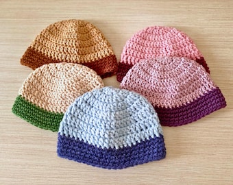 May include: Five crocheted hats in different colors. The hats are all the same style, with a wide brim and a contrasting band around the bottom. The colors are brown, pink, light blue, green, and purple.