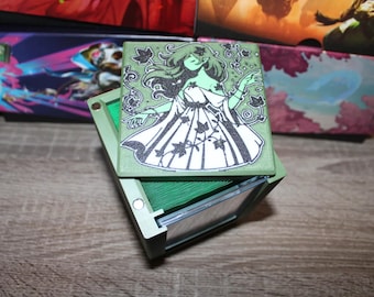 May include: Green card deck box with a clear lid. The lid features a black and white illustration of a woman with long hair and a flowing dress. The woman is surrounded by vines and leaves.
