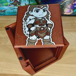 May include: A red-brown, hexagonal box with a hinged lid. The lid features a cartoon illustration of a warrior woman in brown and tan clothing. The box is open, revealing an empty interior.