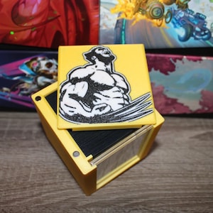 May include: A yellow card holder with a black and white image of a superhero on the lid. The card holder is open and shows a stack of cards inside.