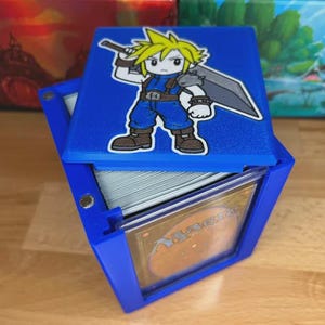 May include: Blue card storage box with a hinged lid. The lid features a cartoon character with a sword. The box is designed to hold trading cards, with a visible card in the front. The box is made of plastic.