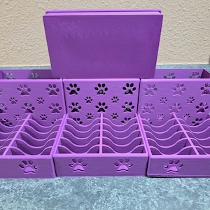 May include: A purple organizer set with paw print cutouts. The set includes three divided trays and a rectangular box. The trays have curved dividers and paw prints on the front and sides. The box sits on top.