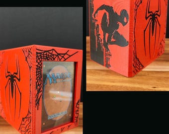 May include: Red and black card storage box featuring Spider-Man graphics. The box has a clear window to display the cards and a black spider web design. The box is designed to hold Magic: The Gathering cards.