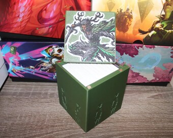 May include: A green cube-shaped box with a removable lid. The lid features a printed image of a character with antlers, wearing a green and black outfit, holding a sword. The box has a design of four figures on each side.