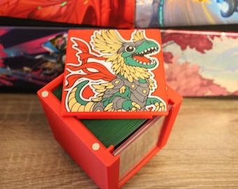 May include: Red card deck box with a green interior and a removable lid featuring a cartoon illustration of a green and yellow dinosaur with red wings and a gray helmet.