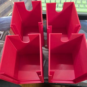May include: Four bright red, rectangular storage containers. Each container has a curved cutout on one side and a small ledge on the other. The containers are made of a solid material and are designed to hold small items.
