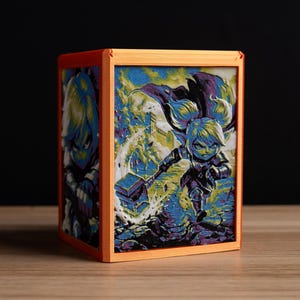 May include: A square orange frame housing a multi-layered 3D art piece featuring a stylized character with light hair and dark armor wielding a large hammer. The artwork displays vibrant blue, purple, and yellow tones with a dynamic action scene.