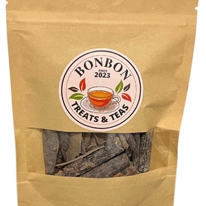 May include: A brown paper bag with a clear window showing dark brown bark pieces. The bag has a logo that says "Bonbon Treats & Teas" with a teacup and the words "Since 2023".