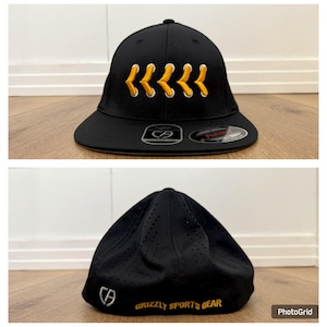 May include: Black baseball cap with a curved peak. The cap has a series of yellow and white stitched arrow designs on the front. The text "GRIZZLY SPORTS GEAR" is printed in yellow on the back of the cap.