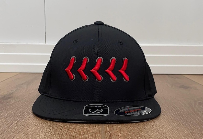 May include: Black baseball cap with a curved peak. The cap has a series of red embroidered chevrons across the front. The cap has a structured fit and a Flexfit brand label.