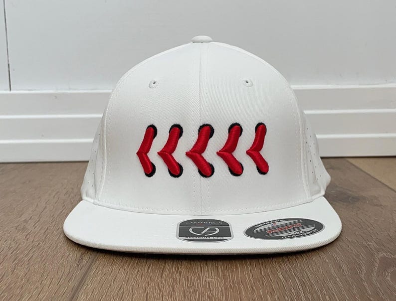 May include: White baseball cap with a flat peak. The cap has red stitching in a repeating pattern across the front. The cap has a structured fit and a curved peak. The cap has a Flexfit tag.