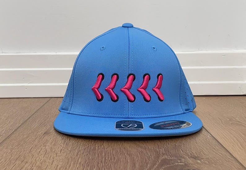 May include: A sky blue baseball cap with a flat peak. The cap has a series of pink embroidered chevrons across the front. The cap has a structured fit and a small logo on the brim.