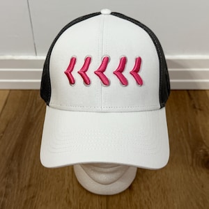 May include: White baseball cap with a black mesh back and a curved brim. The front of the cap features five embroidered pink chevrons. The cap is displayed on a white mannequin head against a wooden background.