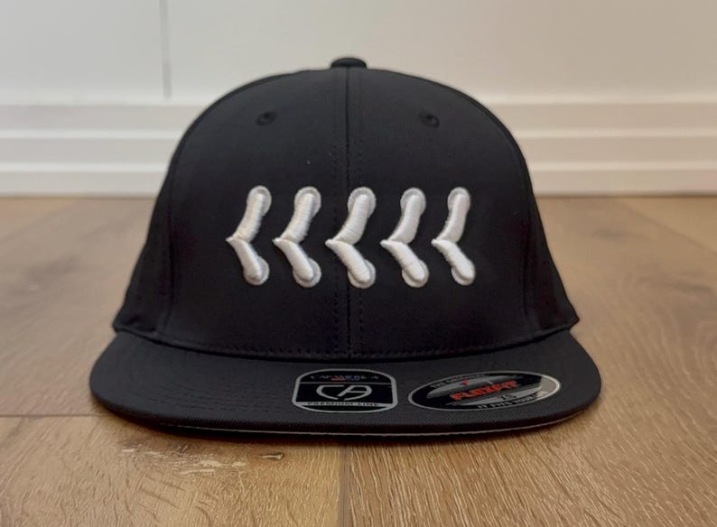 May include: Black baseball cap with a curved peak. The cap has five white, stylized chevrons embroidered across the front. The Flexfit brand logo is visible on the peak.