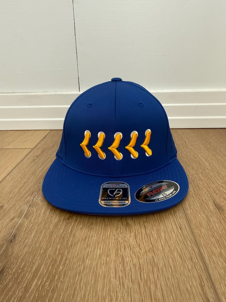 May include: A royal blue baseball cap with a curved peak. The cap has yellow embroidered chevrons across the front and a "Cap America" label. The hat is a Flexfit style.
