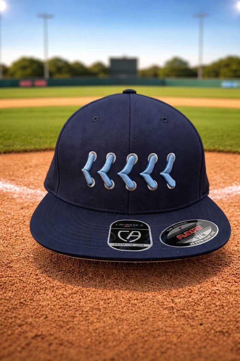 May include: Navy blue baseball cap with light blue embroidered detail. The cap has a curved peak and a structured fit. The cap features a "CAPAMERICA" logo and a "FLEXFIT" sticker.