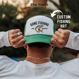 May include: A green and white trucker hat with a fish graphic and the text "Gone Fishing Lake Muskoka".