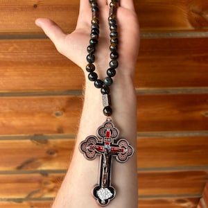 May include: A beaded rosary with a decorative cross pendant. The beads are dark, with brown and blue tones. The cross features a detailed depiction of Jesus Christ and ornate metalwork.