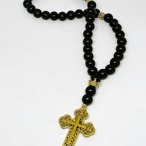 May include: Black beaded rosary with a gold cross pendant. The beads are round and the cross has a detailed design.