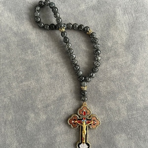 May include: A black beaded rosary with a gold-toned cross pendant. The cross features a depiction of Jesus Christ and is decorated with red and blue enamel.