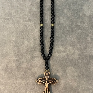 May include: Black beaded rosary with a wooden crucifix featuring a carved figure of Jesus Christ. The crucifix has the inscription "INRI" above the figure and "IC XC" on the crossbeams.
