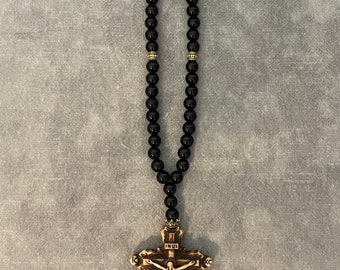 May include: Black beaded rosary with a wooden crucifix featuring a carved figure of Jesus Christ. The crucifix has the inscription "INRI" above the figure and "IC XC" on the crossbeams.