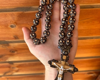 Puede incluir: Un rosario de madera negro con detalles dorados y una cruz de madera detallada. Las cuentas son redondas y tienen un patrón floral.