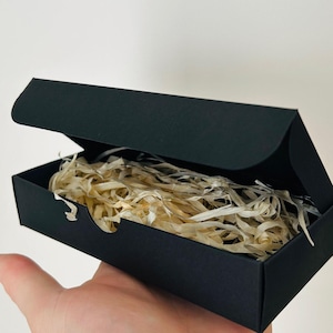 May include: A black rectangular box with an open lid, filled with shredded paper. The word "included" is printed in a white rectangle with a red border. The box is held in a person's hand.