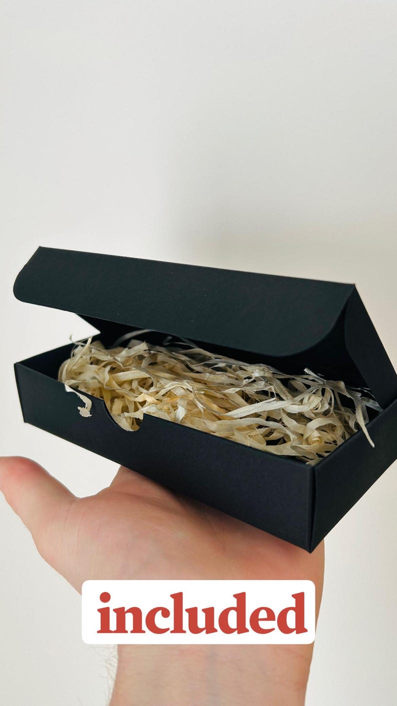 May include: A black rectangular box with an open lid, filled with shredded paper. The word "included" is printed in a white rectangle with a red border. The box is held in a person's hand.