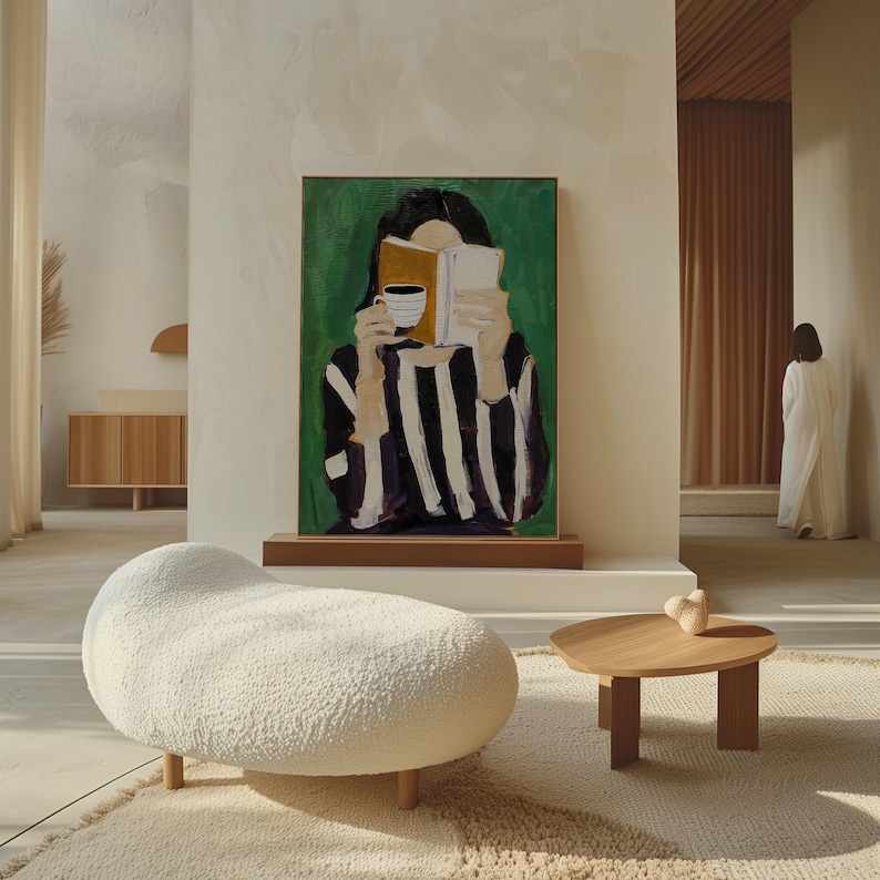May include: An interior scene featuring a modern living room with a large abstract painting of a person reading a book and holding a cup. A white, organic-shaped ottoman and a small wooden table with a decorative object are in the foreground.