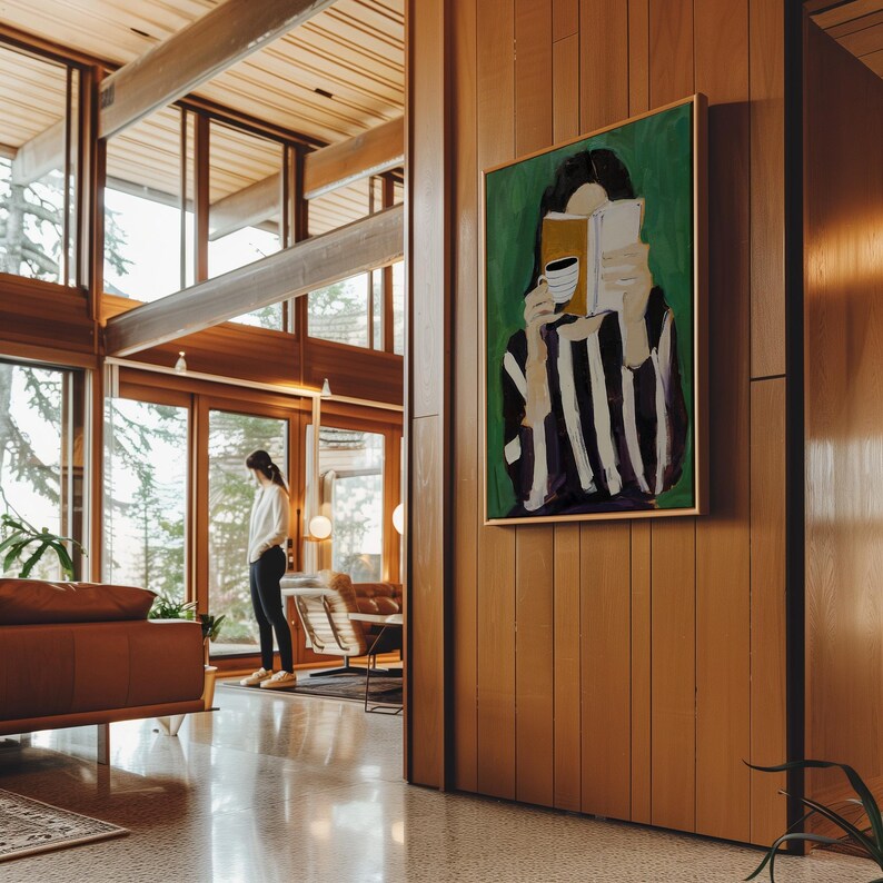 May include: An interior shot of a modern home with large windows and wood paneling. A framed painting on the wall depicts a person reading a book and holding a coffee cup. The painting has a green background and a gold frame. A person is standing in the background.