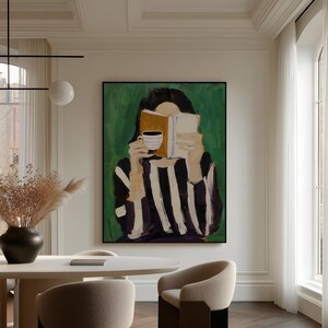 May include: An abstract painting depicts a person reading a book and holding a cup of coffee. The figure is wearing a black and white striped top against a green background. The artwork is framed in black and hangs in a well-lit room.
