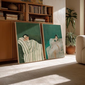 May include: Two framed art prints featuring women in a relaxed setting. One shows a woman resting, draped in a striped robe. The other depicts a woman sipping from a cup. Both have a green background and are in wooden frames.