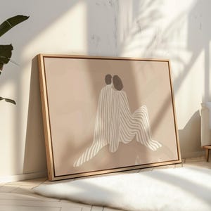 May include: An abstract art print in a wooden frame, depicting two figures in a minimalist style. The figures are in neutral tones with striped patterns, set against a beige background. The artwork evokes a sense of intimacy and comfort.