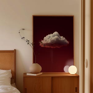 Peut inclure: Une impression d'art encadrée représentant un grand nuage blanc et duveteux sur un fond rouge foncé. Un meuble en bois accueille un vase beige avec une plante, des livres et une lampe sphérique. La scène se déroule dans une chambre.