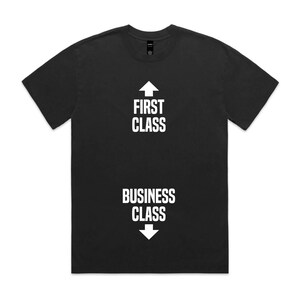 May include: Black t-shirt with white text and arrows. The text reads "FIRST CLASS" with an upward arrow and "BUSINESS CLASS" with a downward arrow. The shirt is a crew neck style.