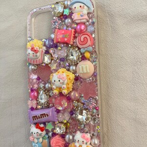 Pu&ograve; includere: Una custodia per telefono rosa decorata con strass, glitter e vari ciondoli, tra cui personaggi di Hello Kitty, caramelle e M&M's.
