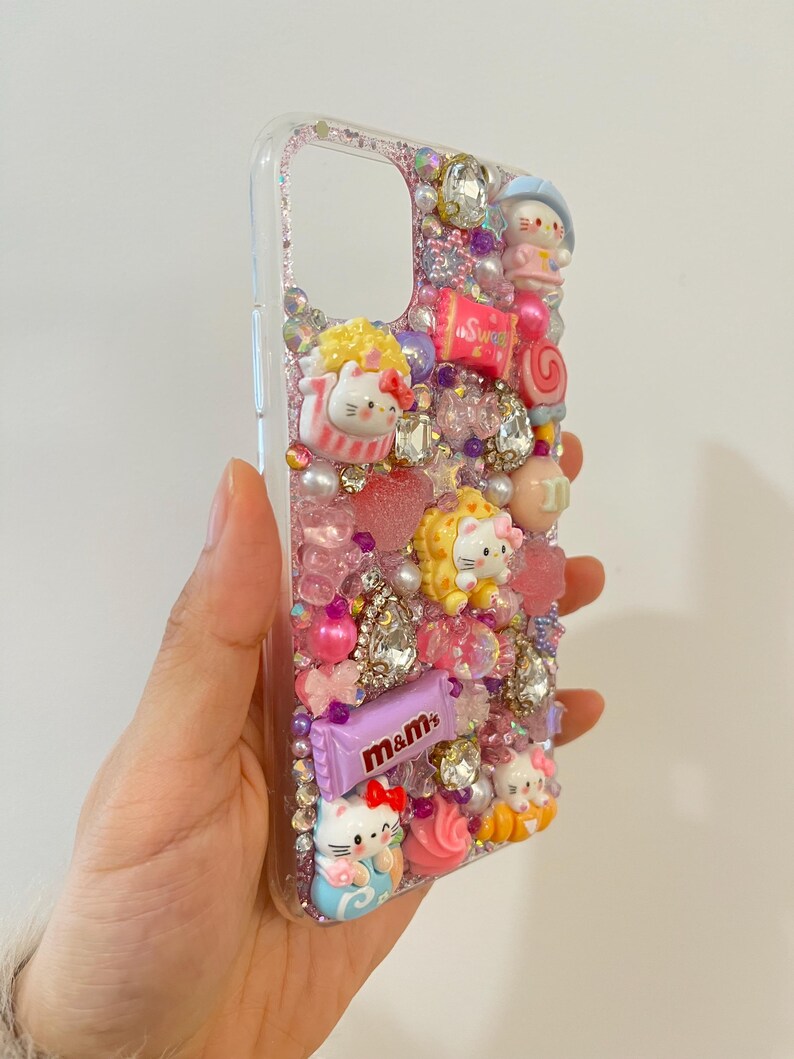 Pu&ograve; includere: Una custodia per telefono rosa e viola con glitter e una variet&agrave; di ciondoli colorati, tra cui personaggi dei cartoni animati, caramelle e strass.