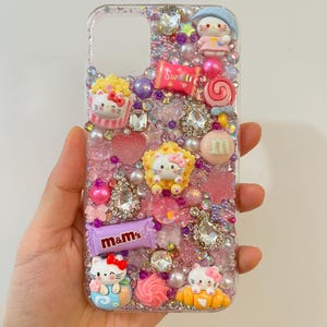 Pu&ograve; includere: Una custodia per telefono trasparente decorata con glitter rosa, viola e bianco, strass e vari ciondoli, tra cui personaggi Hello Kitty, caramelle e una barretta di cioccolato M&M's.