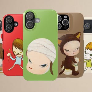 May include: A collection of five smartphone cases featuring stylised illustrations of characters with expressive faces. The designs include a red case, a light green case with a bandaged head character, a brown case, and two cream-coloured cases.