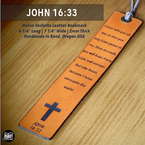 May include: A brown leather bookmark with the text "JOHN 16:33" and a cross. It is made of Italian Vachetta leather and measures 6 1/4 inches long, 1 1/4 inches wide, and 2 mm thick. It is handmade in Bend, Oregon, USA.