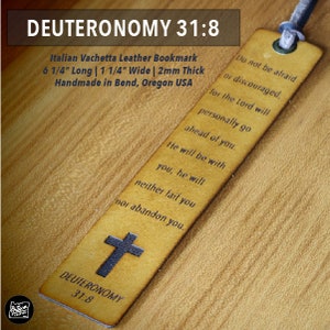 May include: A brown leather bookmark with a cross and the text "DEUTERONOMY 31:8" printed on it. The bookmark is 6 1/4 inches long, 1 1/4 inches wide, and 2 millimeters thick. It is handmade in Bend, Oregon, USA. The bookmark has the text "Do not be afraid or discouraged, for the Lord will personally go ahead of you. He will be with you, he will neither fail you nor abandon you." printed on it.