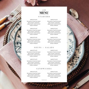 May include: A printed menu with the text "MENU" and "STARTERS", "SOUPS + SALADS", and "SANDWICHES". The menu is on a white background, with a floral patterned plate and silverware in the background.