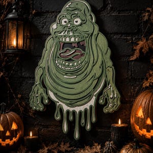 May include: A layered wooden wall art piece depicting a green, ghost-like creature with a wide, open mouth, large eyes, and dangling, dripping limbs. The design features multiple stacked levels of wood in shades of green, white, and dark red.
