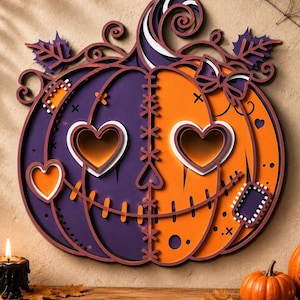Puede incluir: Una decoración de pared de madera en capas con forma de calabaza, dividida verticalmente en mitades morada y naranja. Presenta ojos en forma de corazón, una boca cosida, un lazo y detalles de hojas decorativas en el diseño.