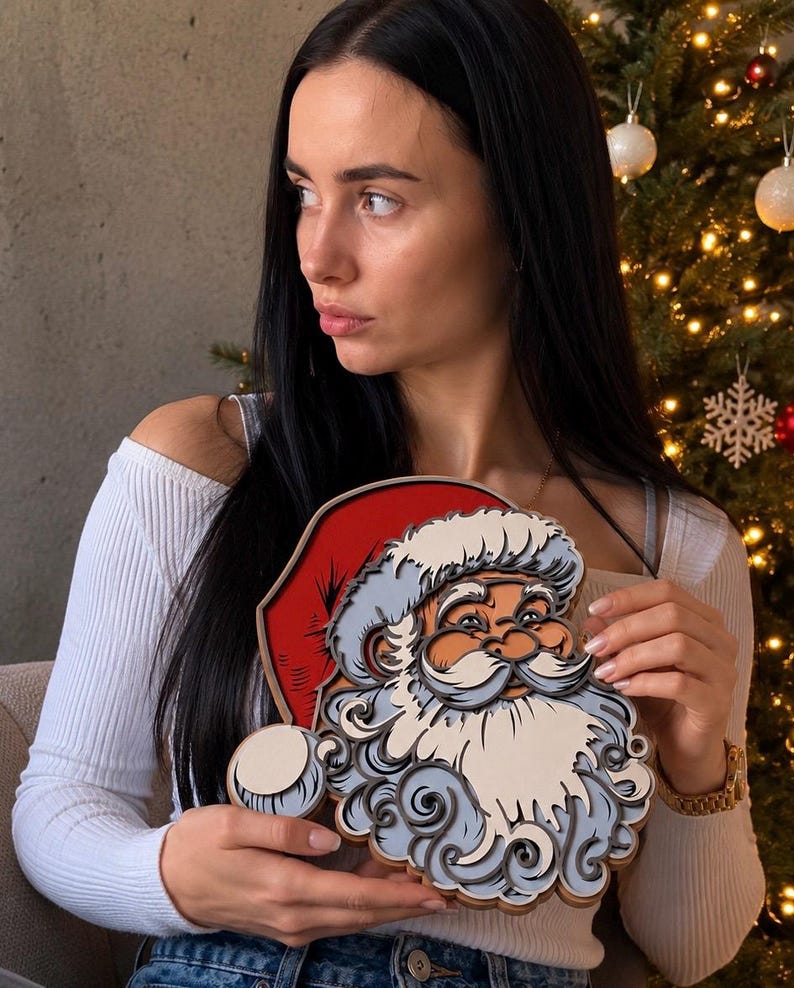 May include: A layered wooden wall art piece depicting the face of Santa Claus with a red hat, a white mustache, and a detailed beard. The design features stacked cutouts in shades of red, white, light blue, and dark gray, creating a dimensional effect.