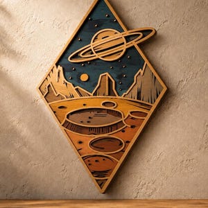 May include: A diamond-shaped wooden wall art piece featuring a layered space scene. The design includes a dark blue sky with a ringed planet, a small sun, and rocky mountains above a textured orange and brown cratered planetary surface.